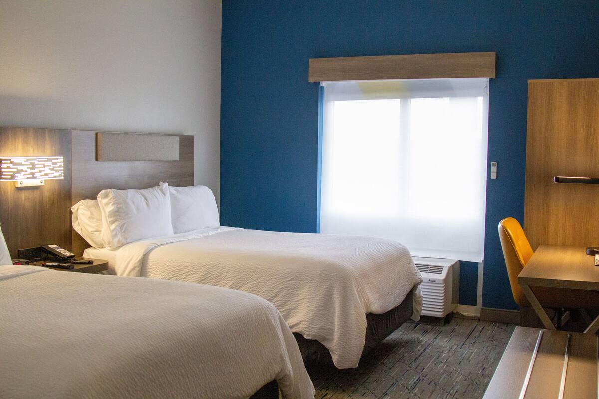 A hotel room with two beds, a desk, and a window with blinds.