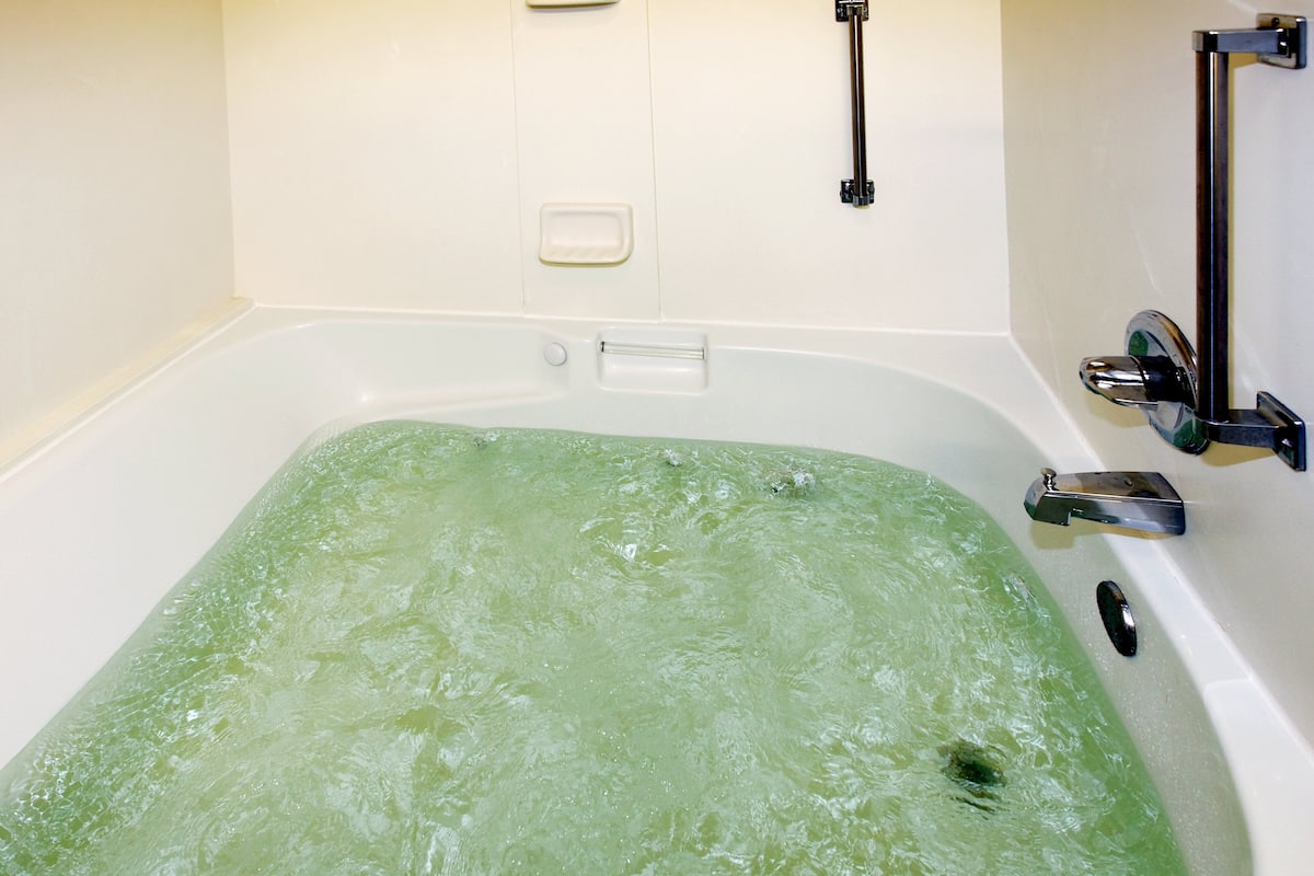 A bathtub with green water, a soap dish, and a handrail.