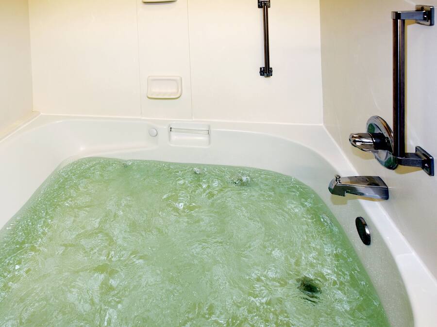 Une baignoire remplie d’eau verte, un porte-savon et une barre d’appui.