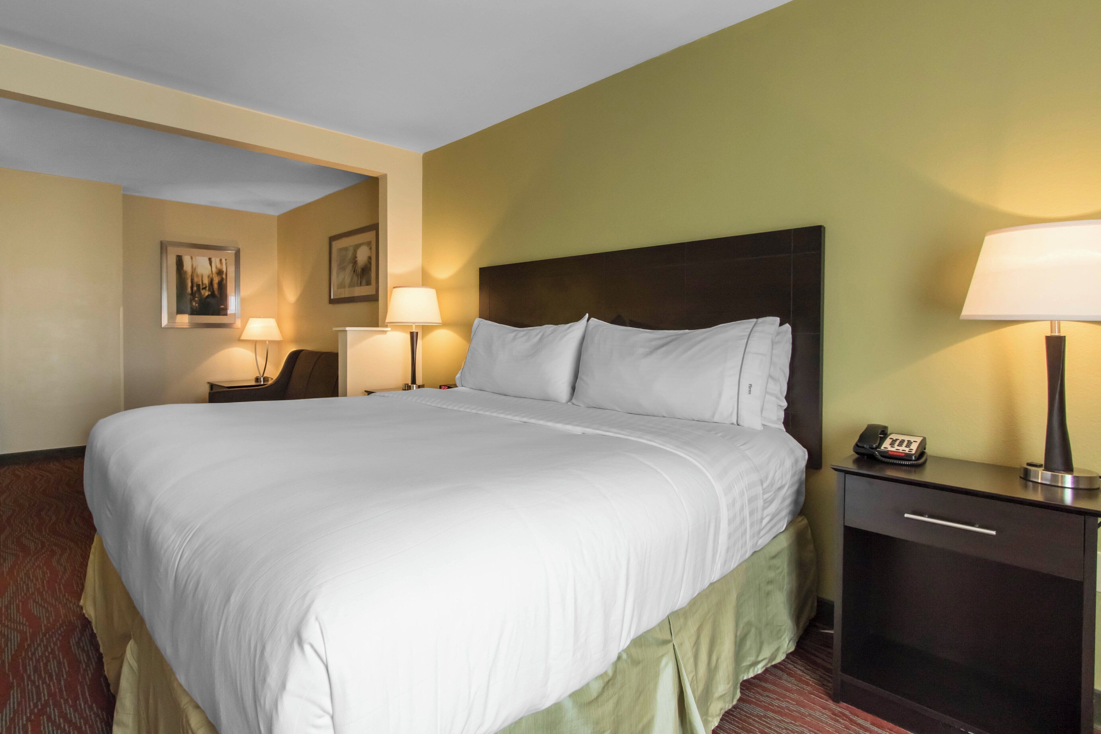 A hotel room with a large bed, two bedside tables with lamps, a nightstand with a phone, and a wall-mounted picture.