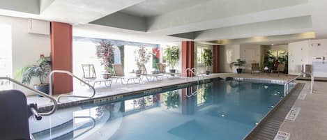 An indoor swimming pool with clear water, surrounded by lounge chairs and potted plants.