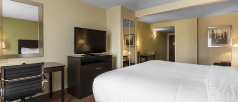 Habitación de hotel con una cama grande, un escritorio con silla, un televisor y un espejo.