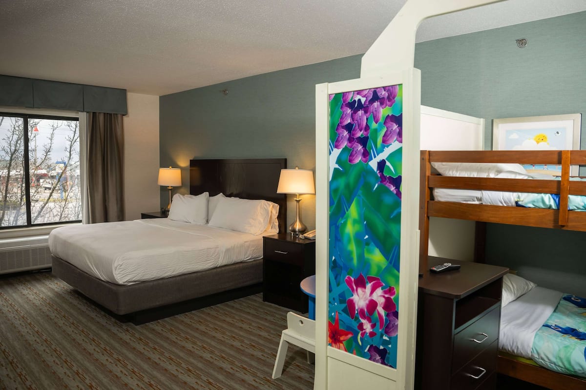 A hotel room with a large bed, a desk with a chair, a bunk bed, and a window with curtains.