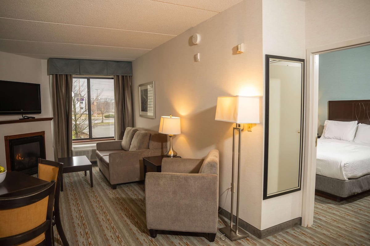 A hotel room with a sofa, armchair, bedside table, lamp, and a bed.