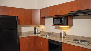 A compact kitchen with wooden cabinets, a black refrigerator, a microwave, a coffee maker, and a dishwasher. - Wyndham Garden Erie (Erie)