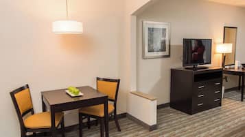 Ein Hotelzimmer mit Esstisch, zwei Stühlen, einem Fernseher, einem Schreibtisch mit Lampe und einem gerahmten Bild an der Wand.