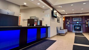 A hotel reception area with a blue-lit counter, a fireplace, and a television mounted on the wall. - Wyndham Garden Erie (Erie)