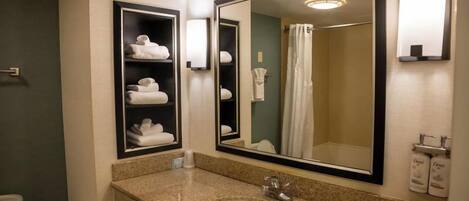 A hotel bathroom with a large mirror, a sink, and shelves with folded towels.