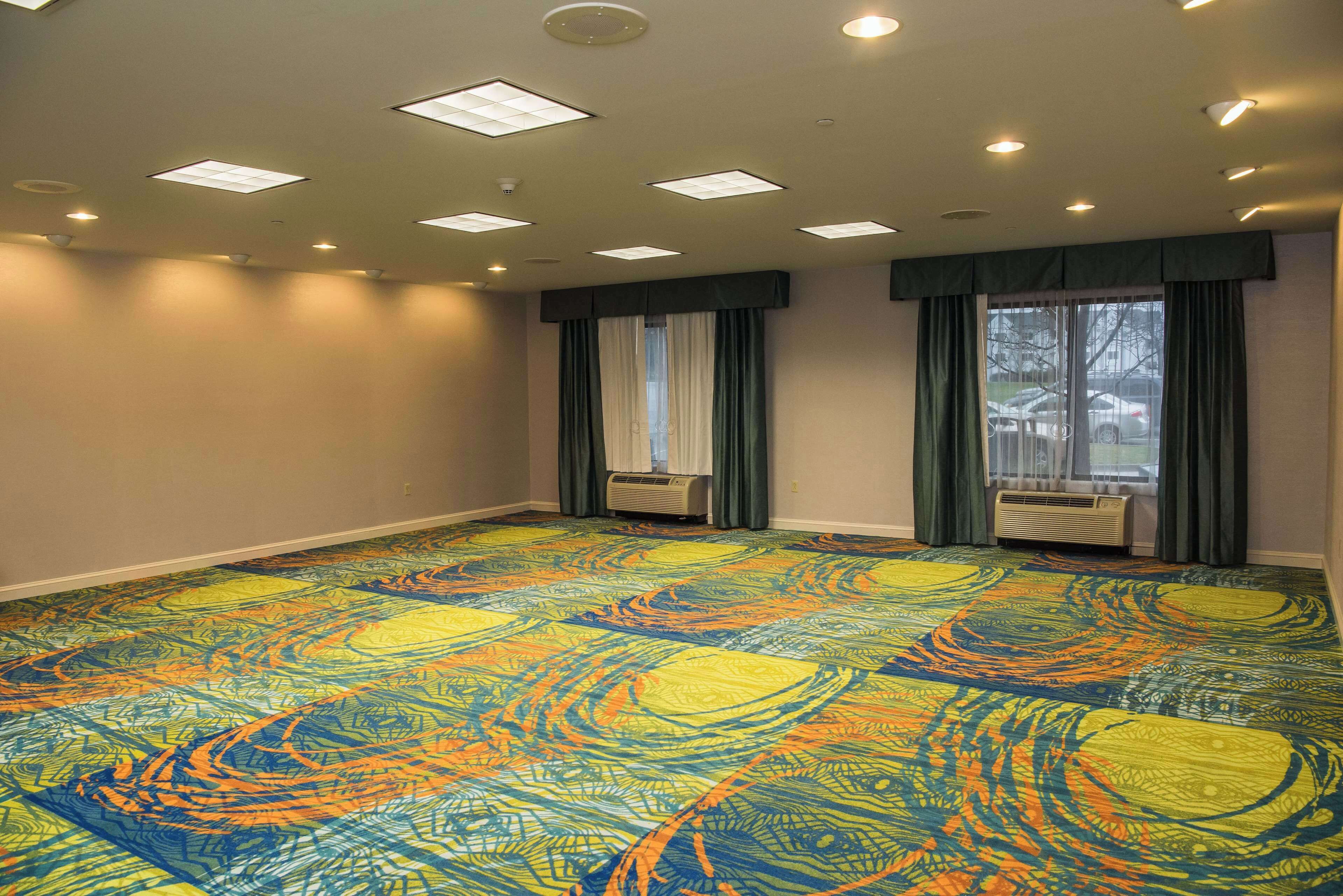 A large, empty room with a colorful carpet, air conditioning units, and windows with curtains.
