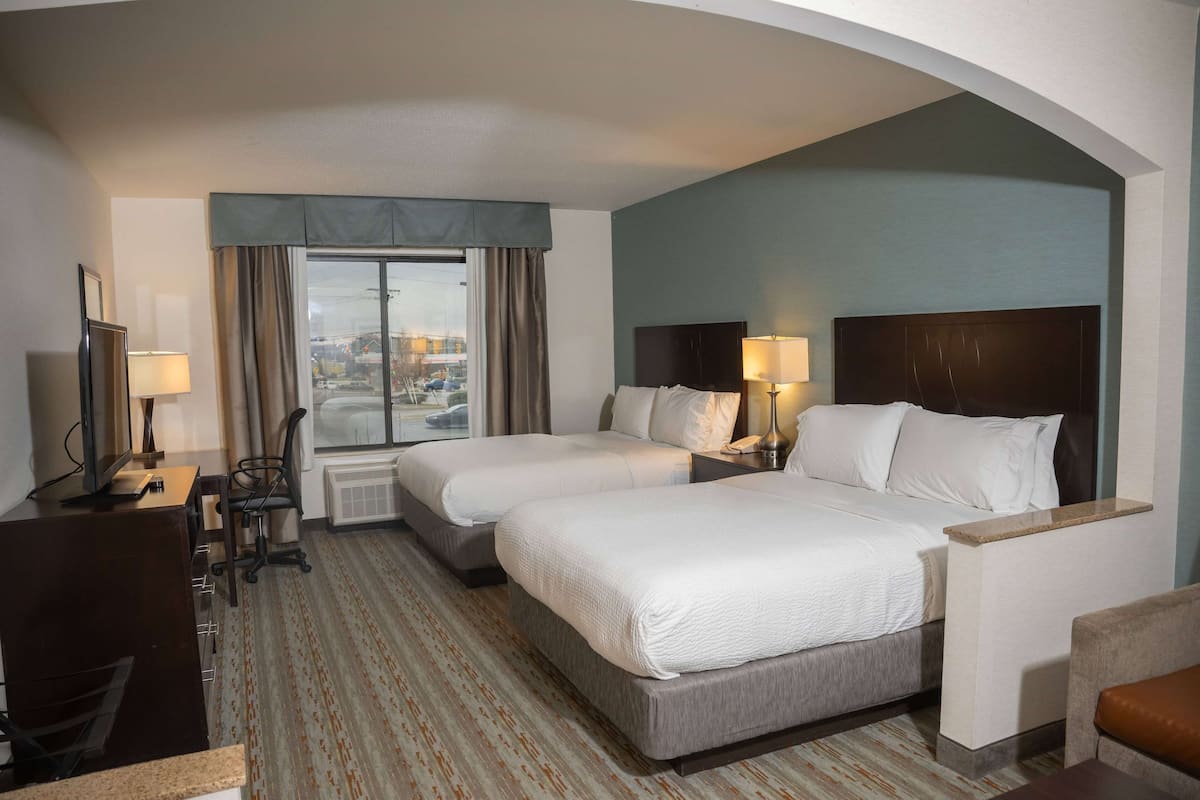 A hotel room with two beds, a desk, a chair, and a view of the city.