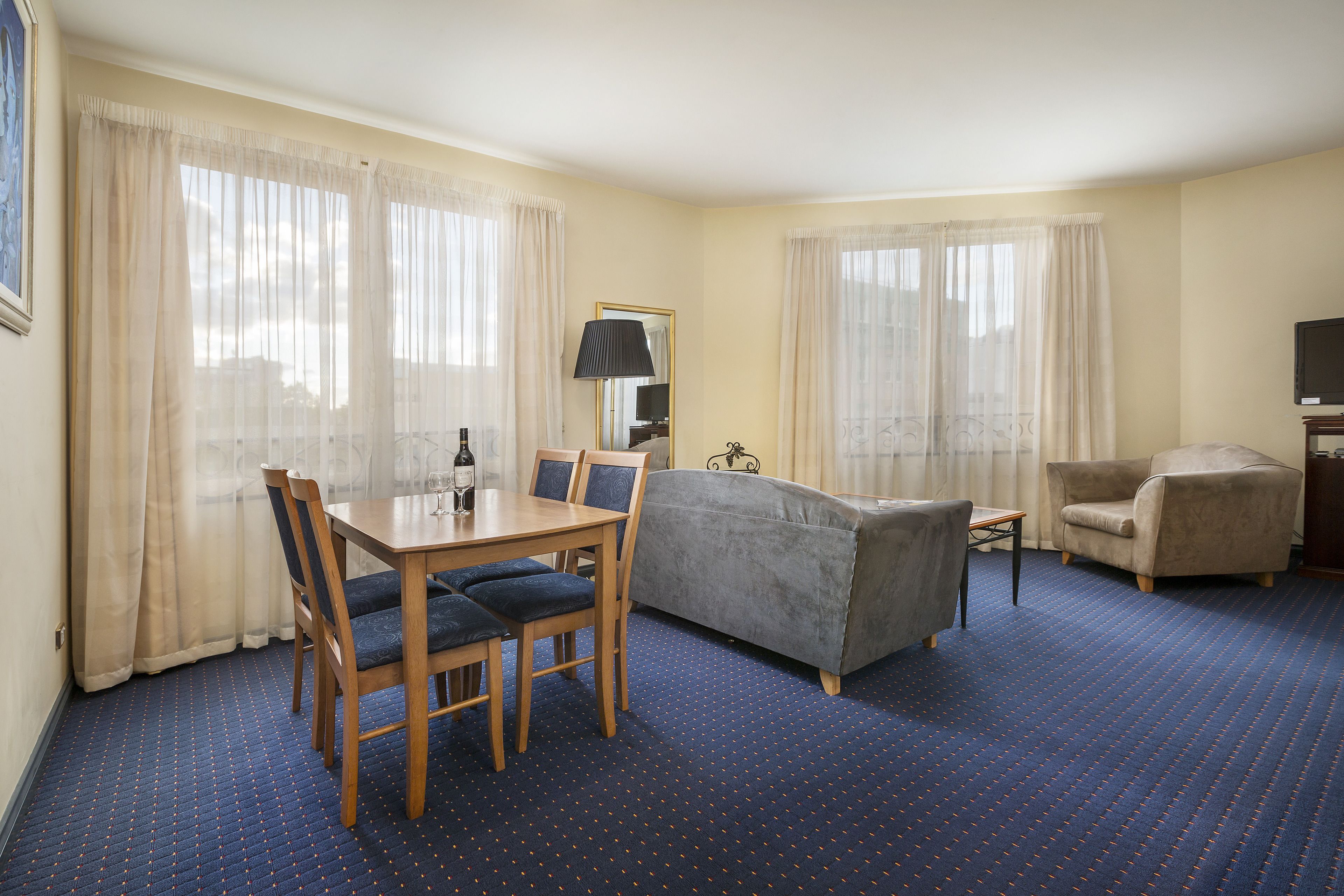 A hotel room with a dining table, chairs, a sofa, and a TV.