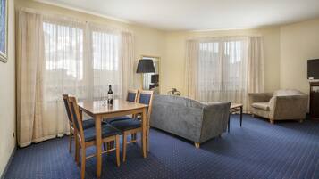 A hotel room with a dining table, chairs, a sofa, and a TV.