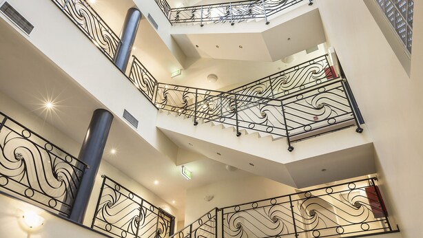 Un intérieur à plusieurs niveaux, agrémenté de rampes noires décoratives, d’une colonne centrale et d’un plafond en verre qui laisse entrer la lumière naturelle.