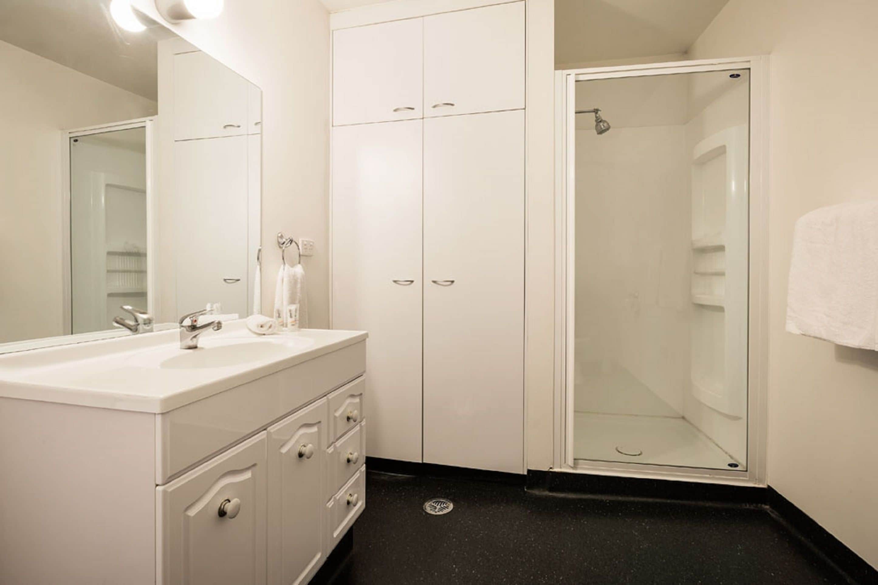 A bathroom with a white vanity, a glass shower enclosure, and a white towel hanging on the wall.
