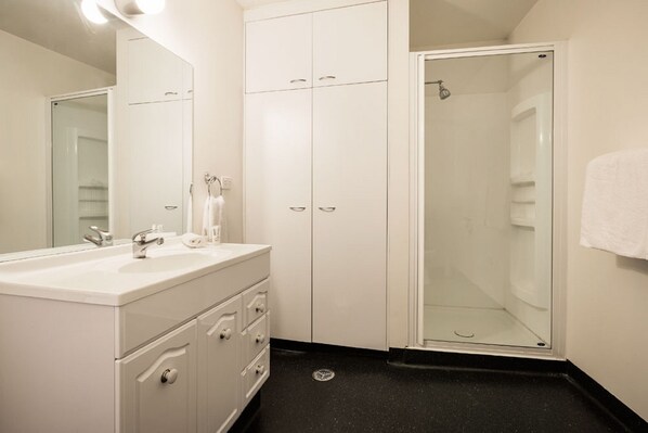 A bathroom with a white vanity, a glass shower enclosure, and a white towel hanging on the wall. - Quest Savoy (Hobart)