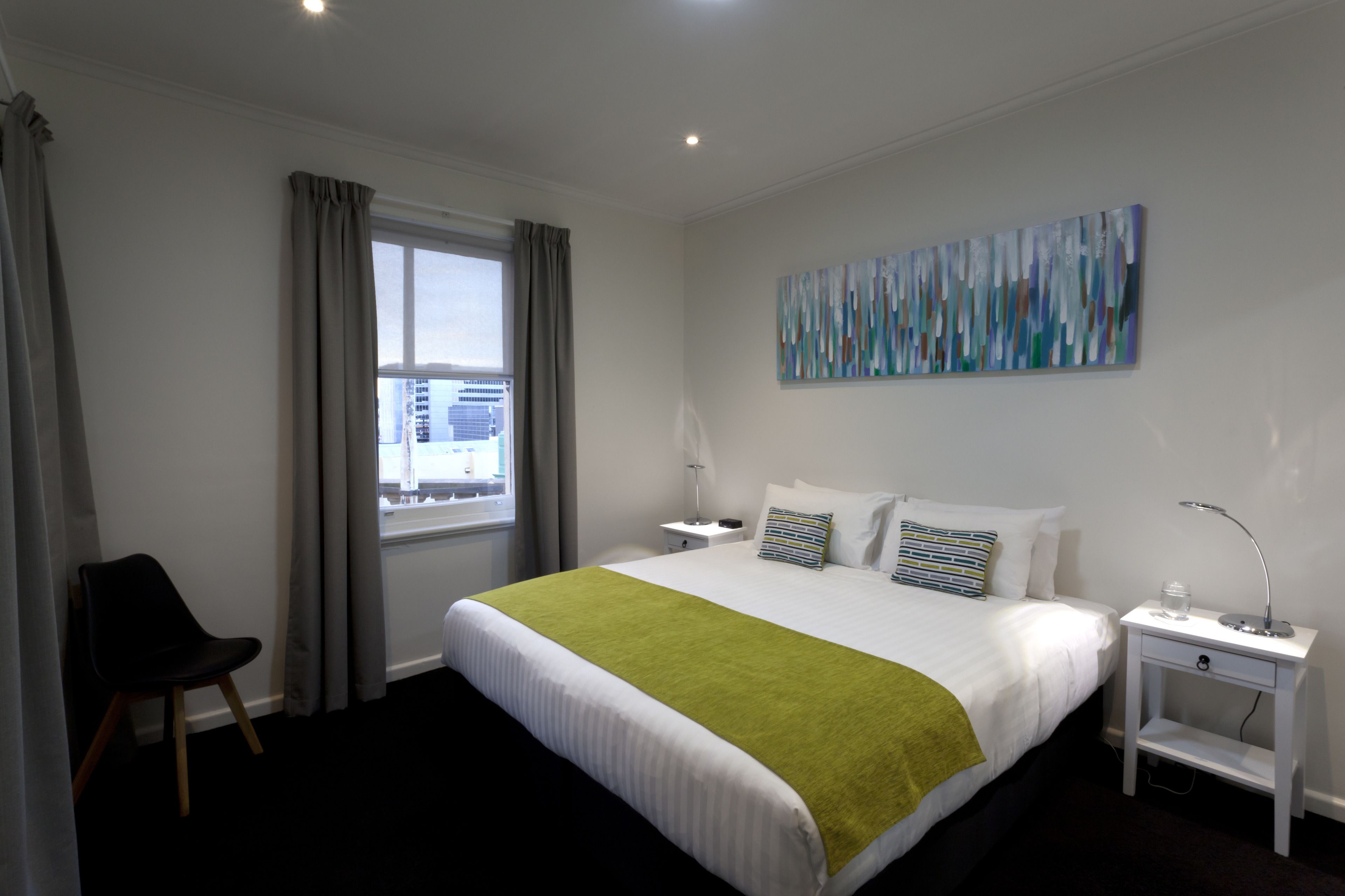 Une chambre d’hôtel avec un lit, une chaise, une table de chevet, une lampe et un tableau au mur.