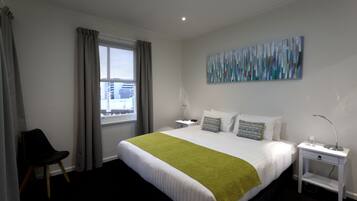 Une chambre d’hôtel avec un lit, une chaise, une table de chevet, une lampe et un tableau au mur.