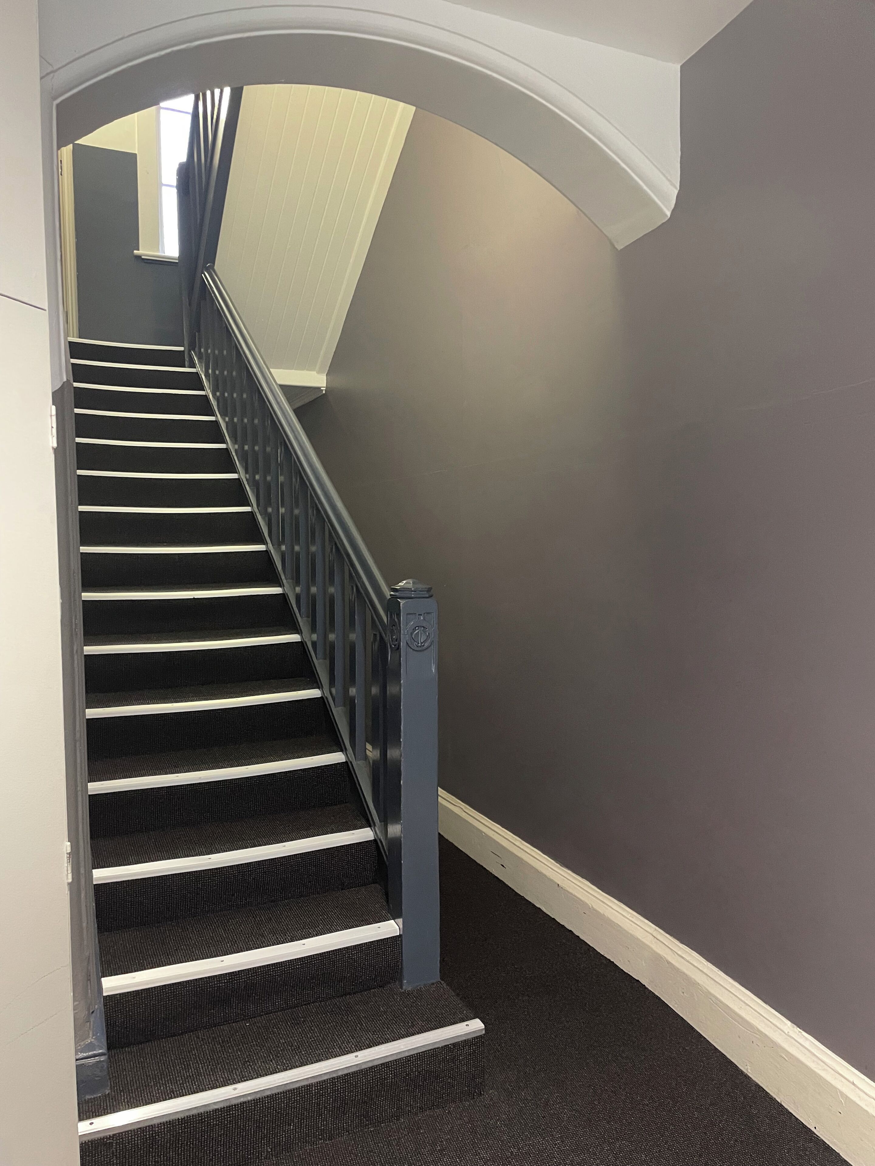 Eine Treppe mit Handlauf, Teppichstufen und einer dunklen Wand.