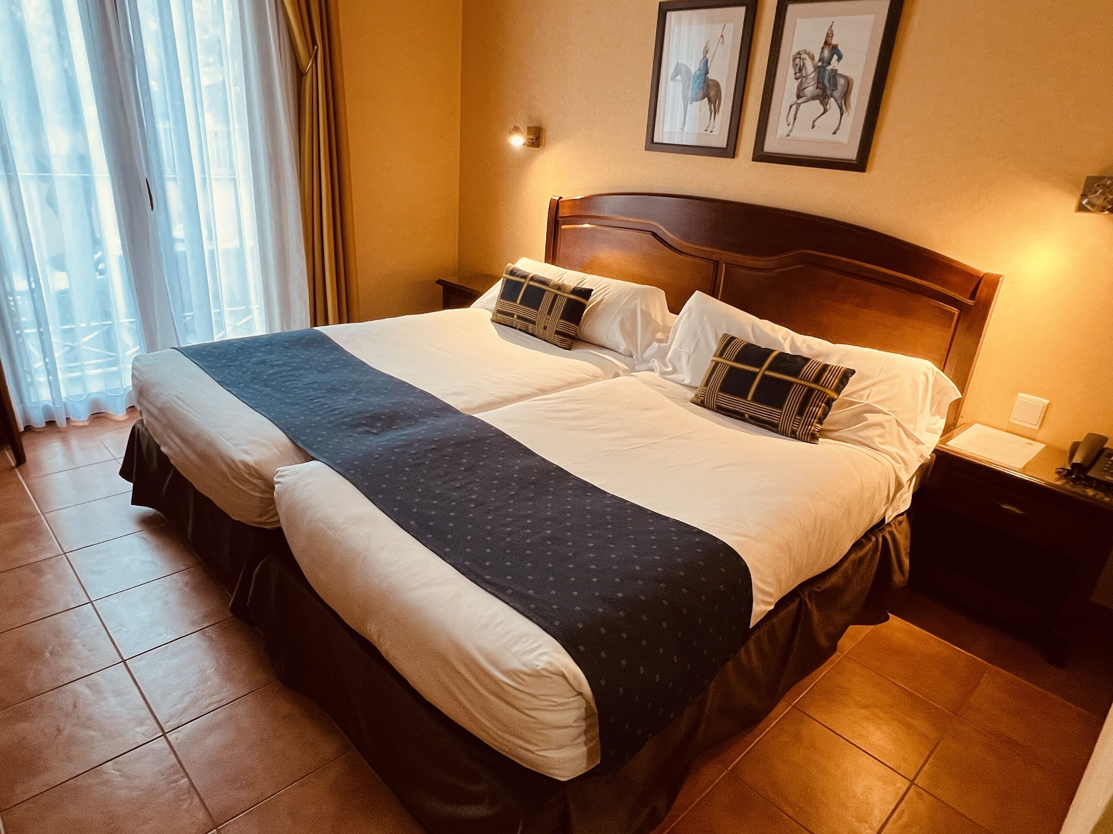 A double bed with a dark blue bedspread, white pillows, and a wooden headboard. There are two framed pictures on the wall above the bed.