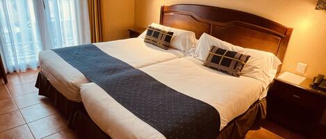A double bed with a dark blue bedspread, white pillows, and a wooden headboard. There are two framed pictures on the wall above the bed.