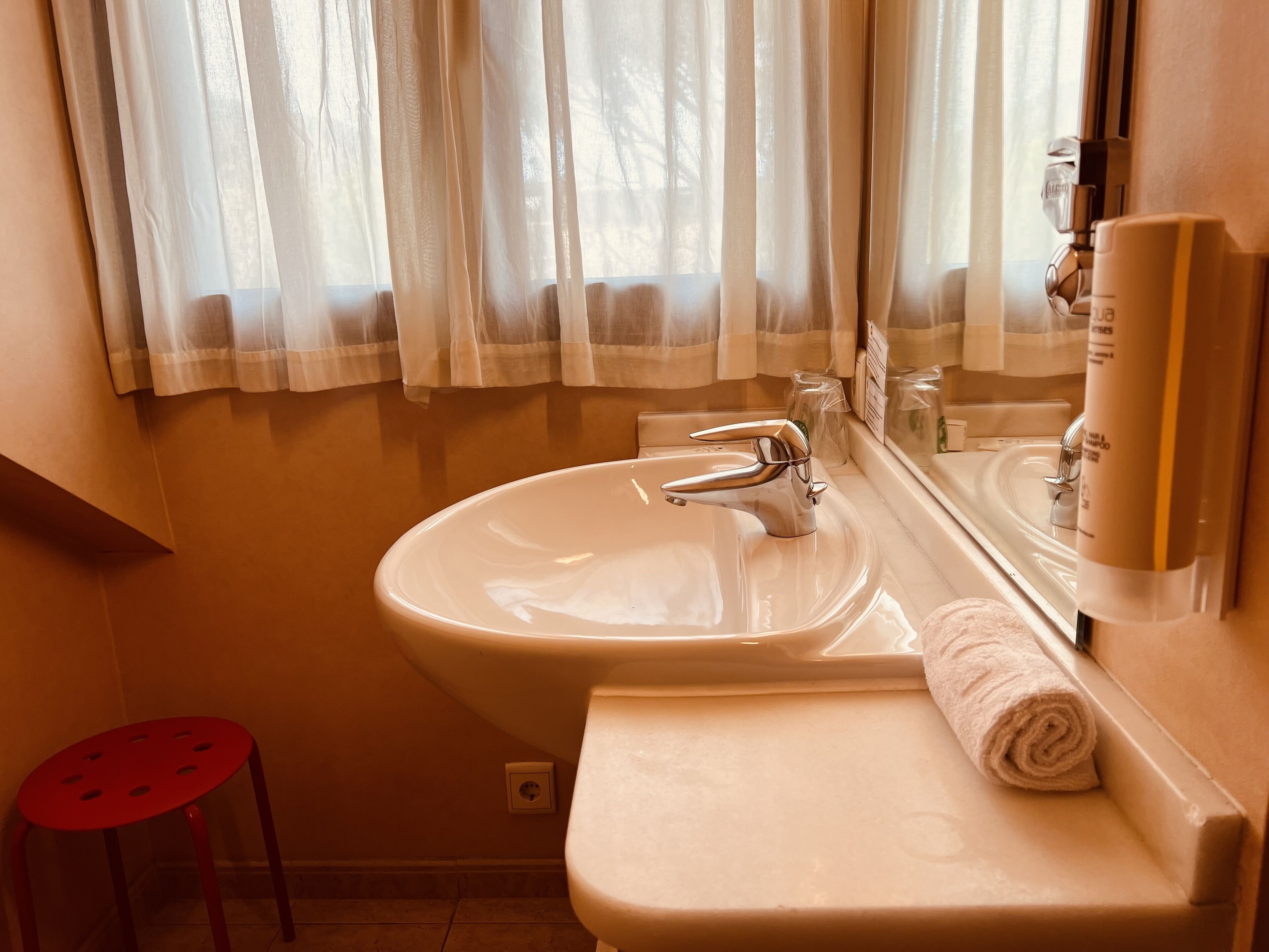 A bathroom with a sink, mirror, and a red stool.