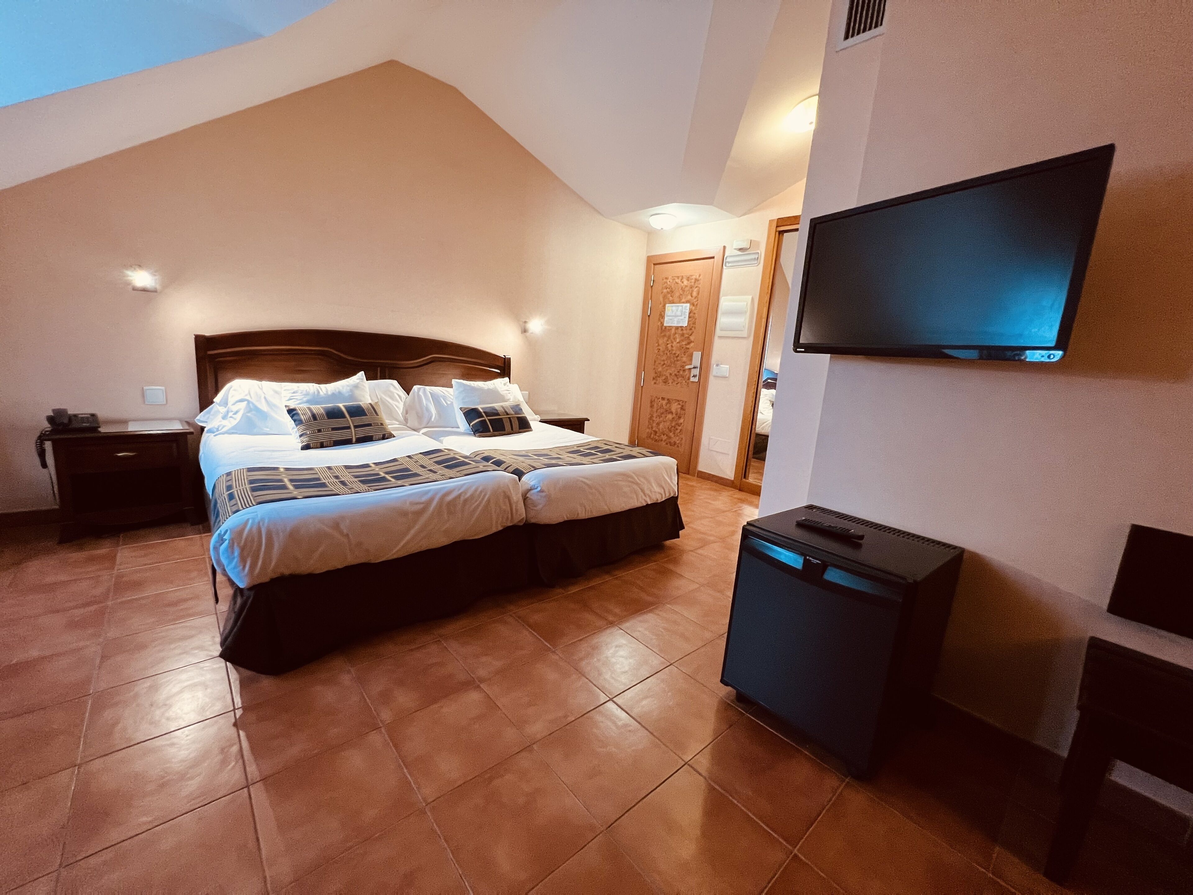 Un dormitorio con una cama grande, un televisor montado en la pared y un escritorio pequeño con una lámpara.