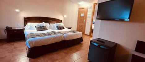 Un dormitorio con una cama grande, un televisor montado en la pared y un escritorio pequeño con una lámpara.