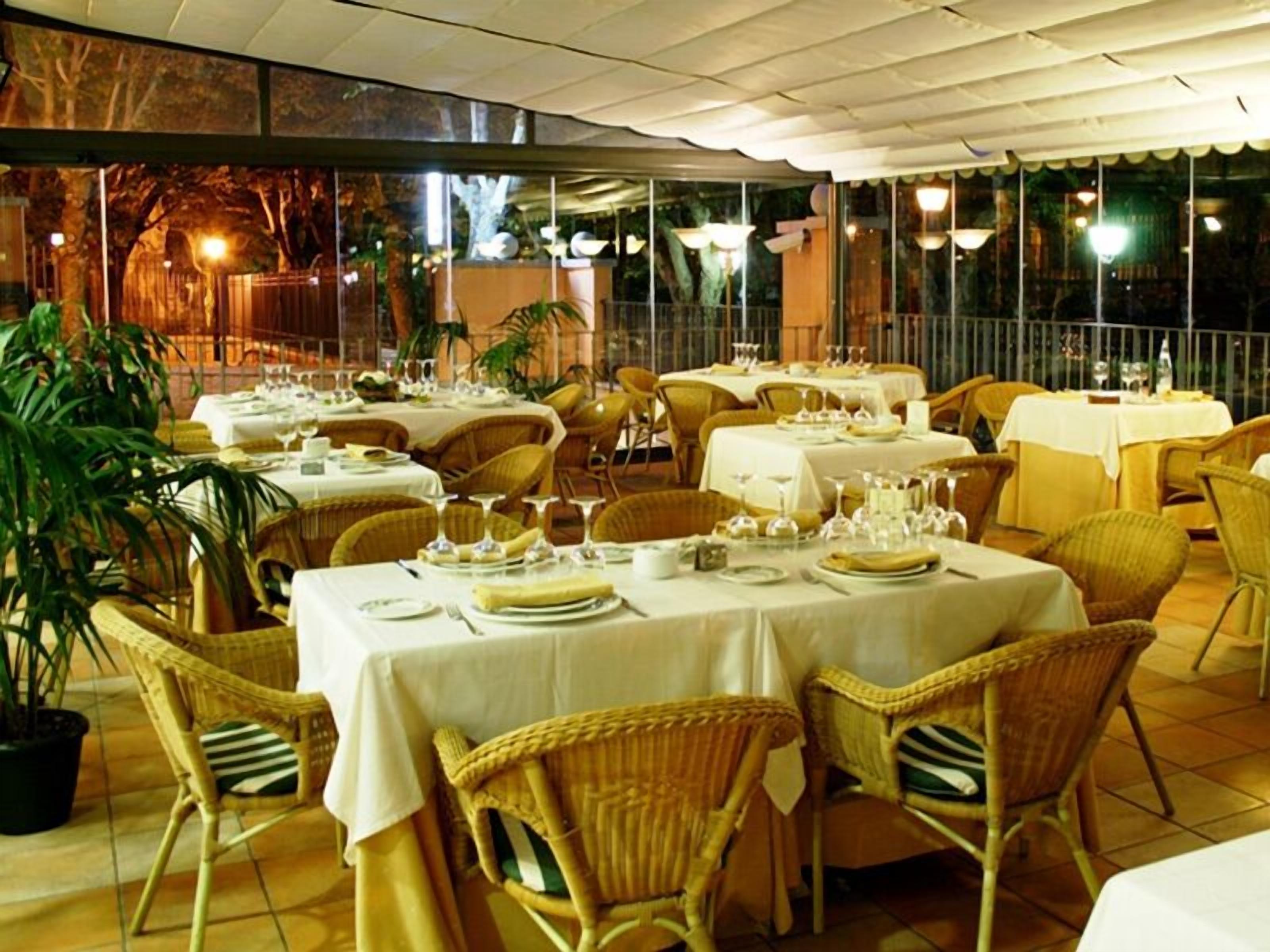 Un restaurante con mesas dispuestas para comer, sillas de mimbre y plantas en macetas.