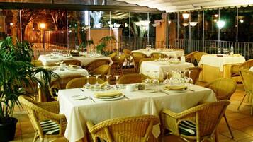 Un restaurante con mesas dispuestas para comer, sillas de mimbre y plantas en macetas.