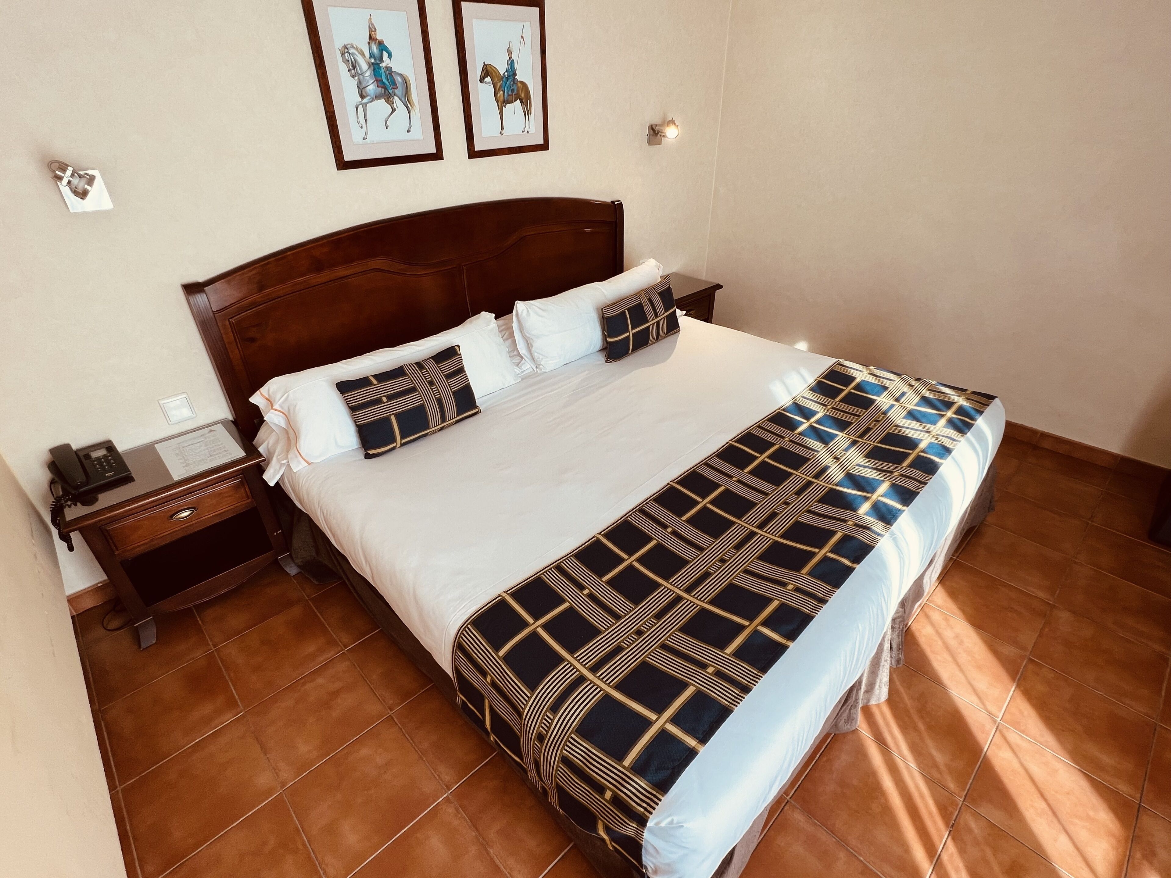 Una cama bien hecha con una colcha estampada, un cabecero de madera y dos lámparas fijadas a la pared.