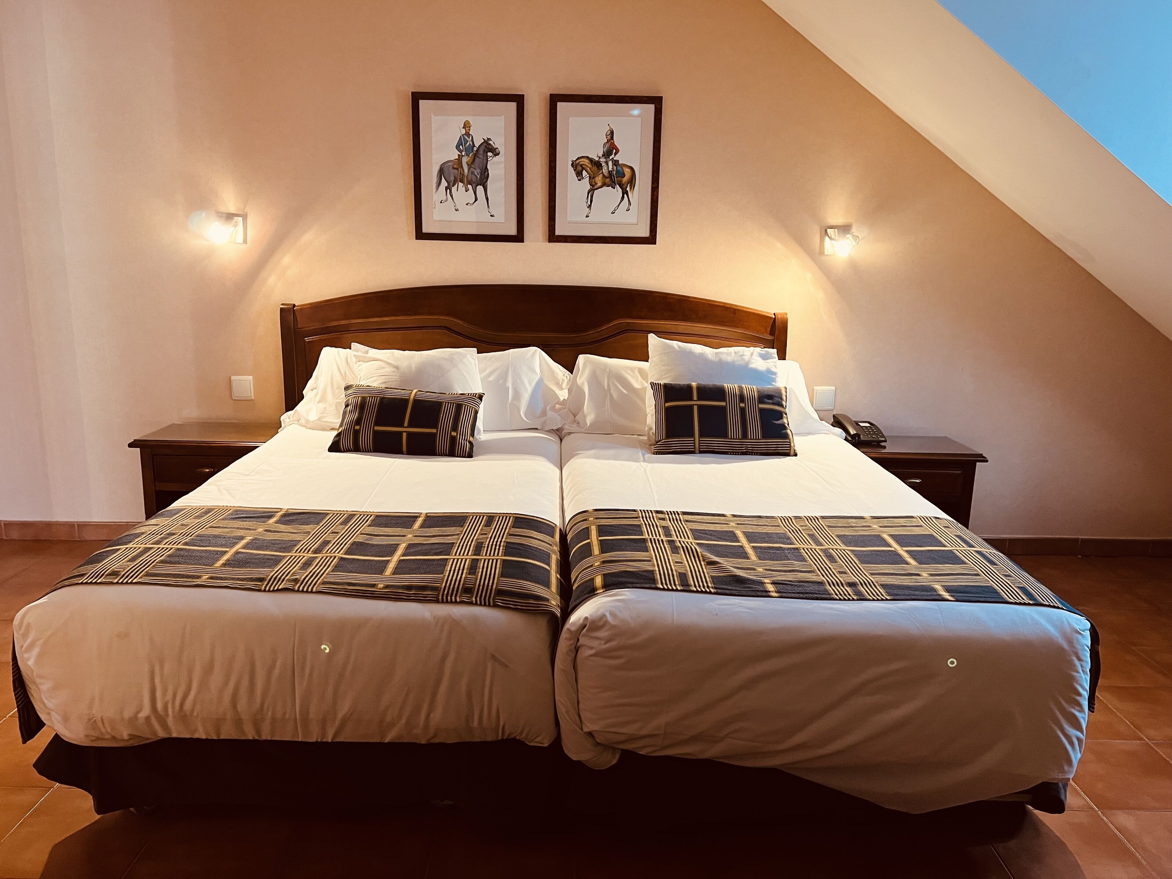 A double bed with a wooden headboard, two bedside tables, and two framed pictures on the wall.