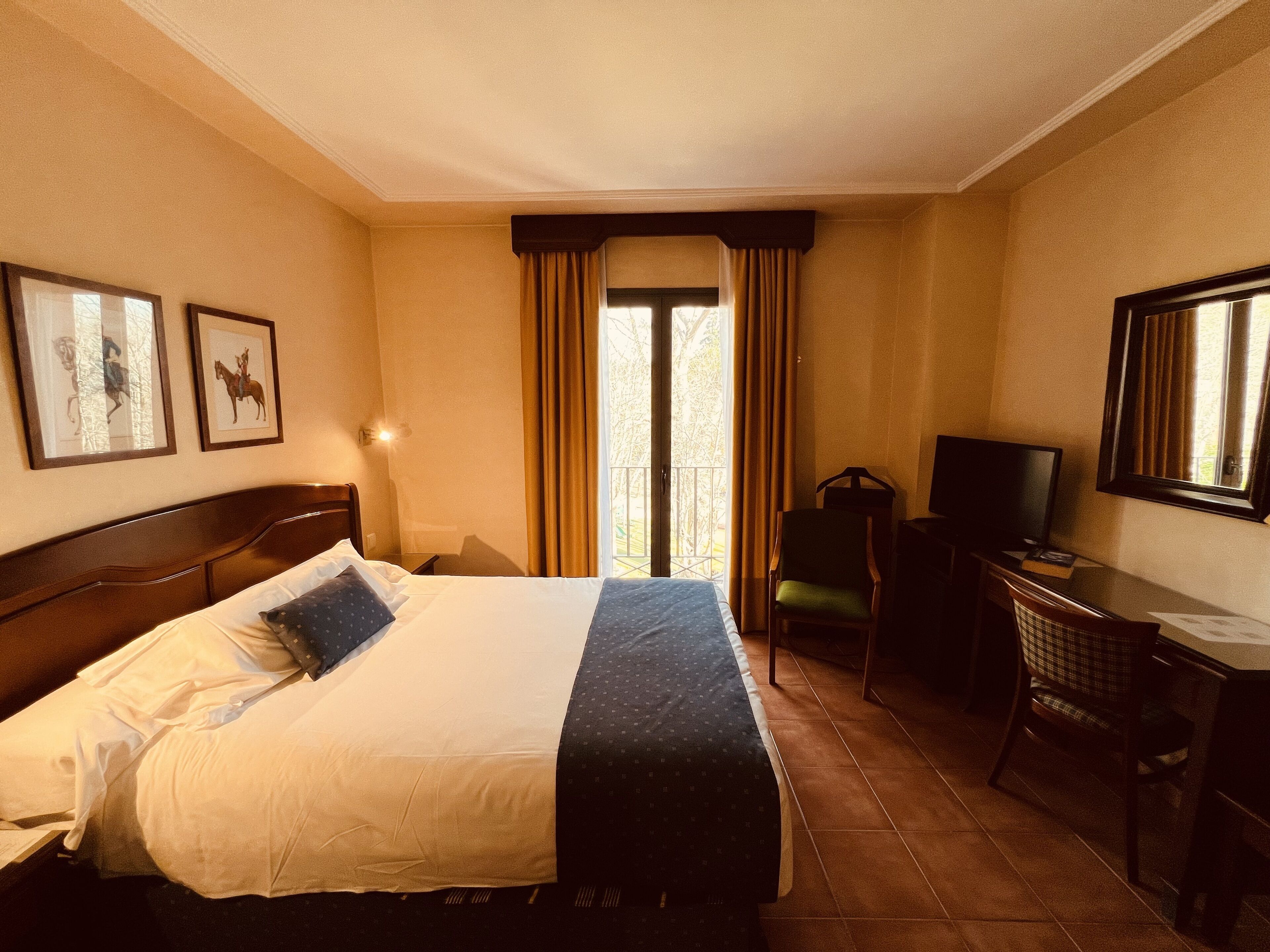 A hotel room with a large bed, a desk with a chair, a television, and a window with curtains.