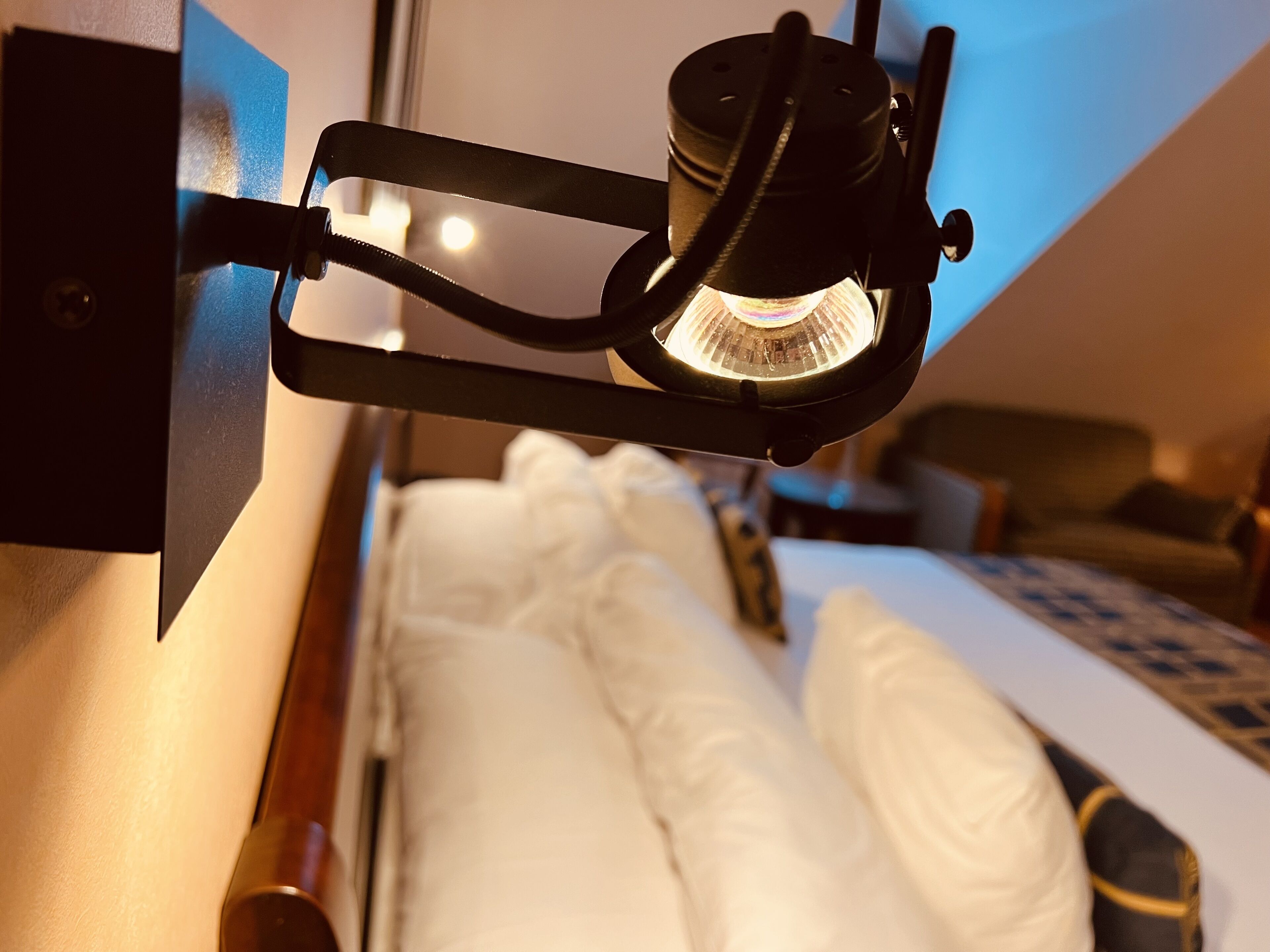 Uma cama com roupa de cama branca, uma cabeceira e uma mesinha de cabeceira com um abajur.