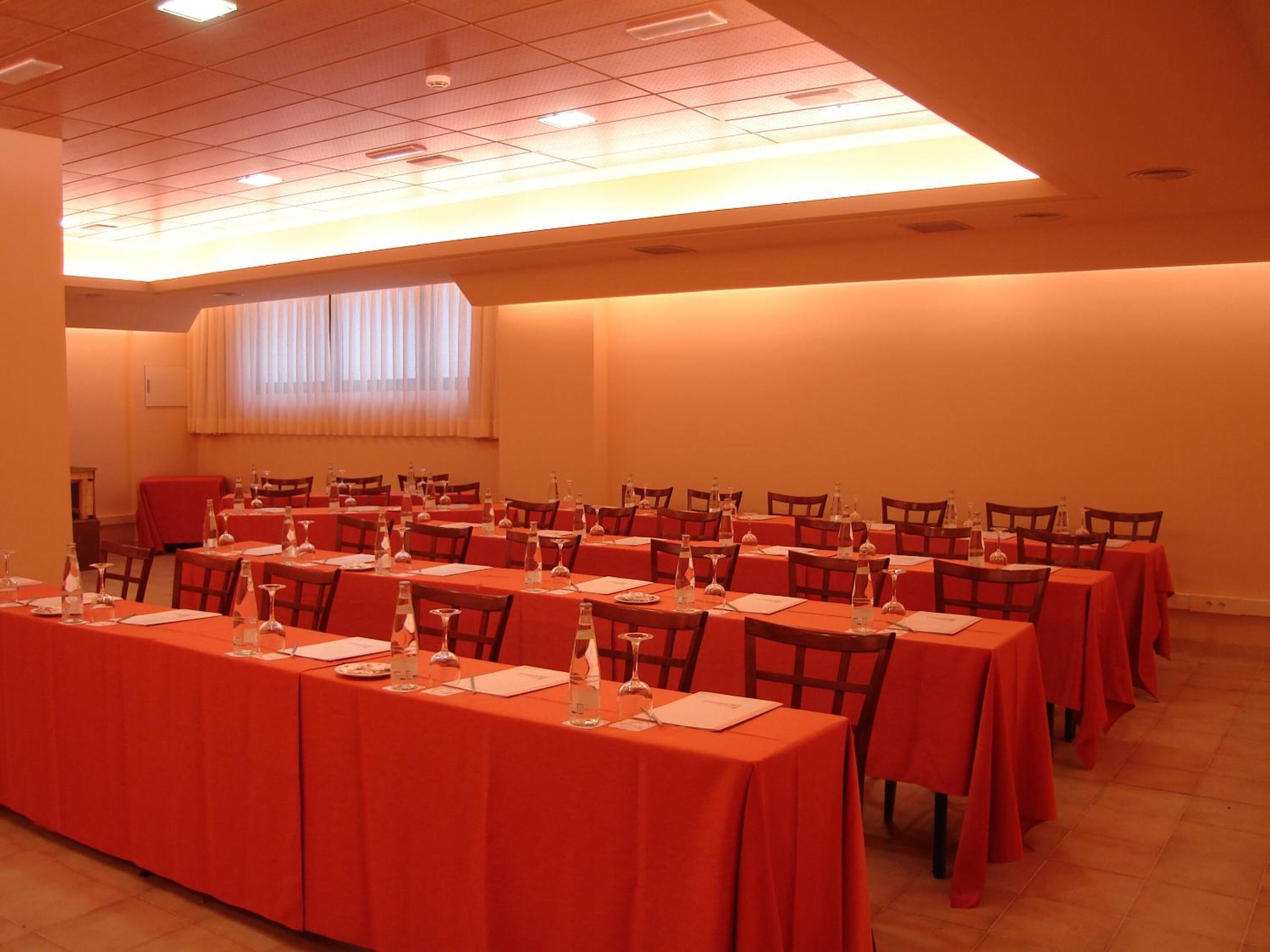 Un salón de conferencias con varias mesas, cada una con botellas de agua, vasos y blocs de notas.