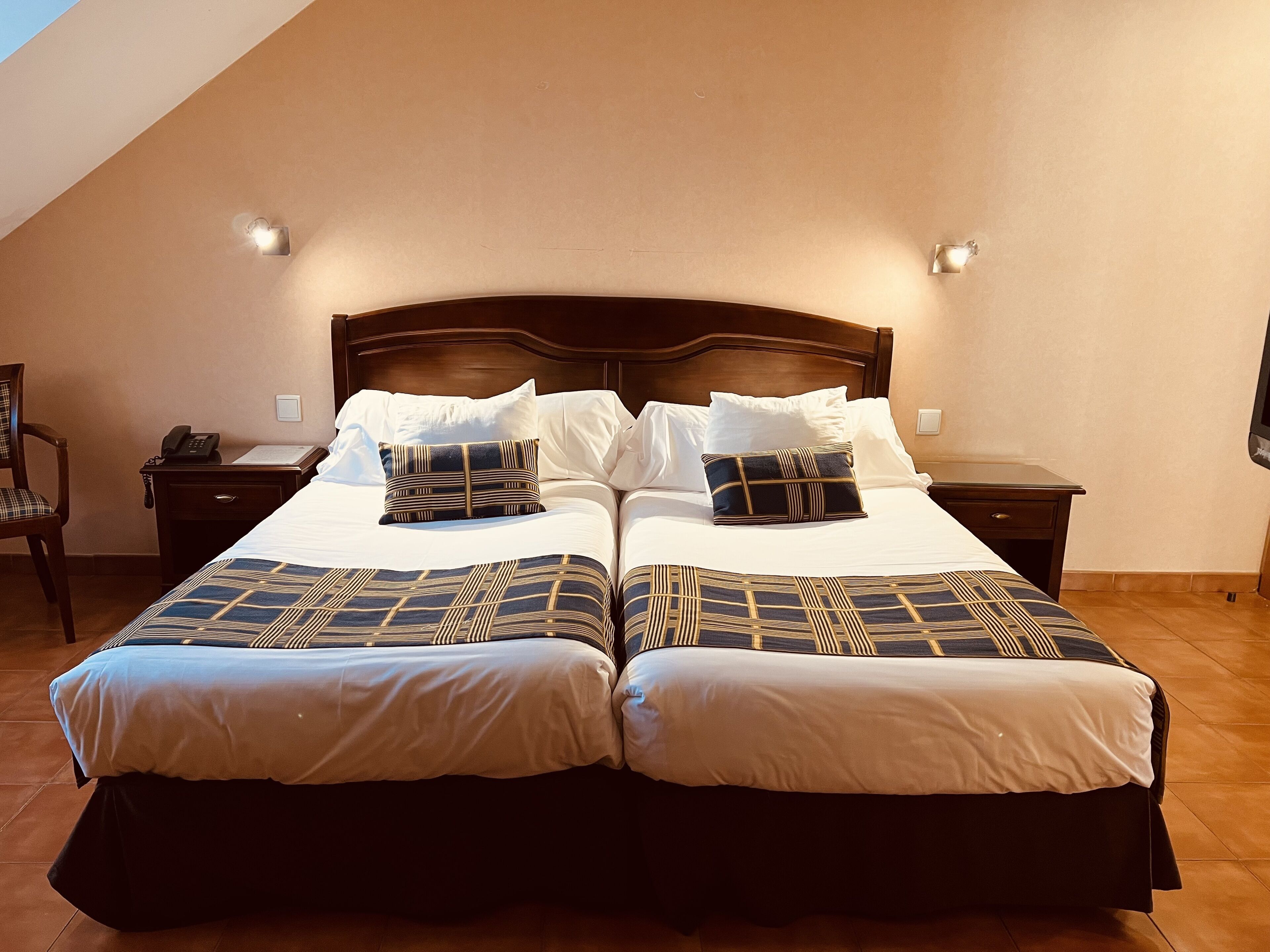 A double bed with a wooden headboard, two bedside tables, and a nightstand with a phone.
