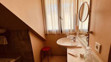 Baño con lavamanos, espejo y ventana con cortinas. Se observa un taburete rojo y un perchero.