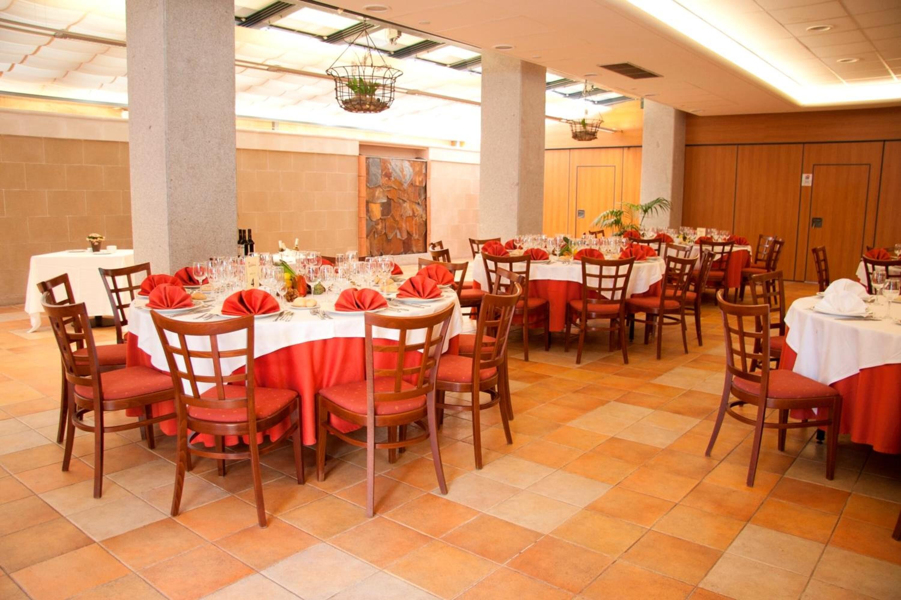 Une salle de banquet avec des tables rondes, des nappes rouges et des chaises en bois.