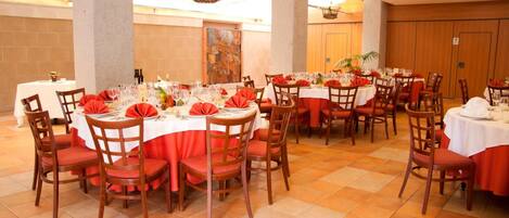 A banquet hall with round tables, red tablecloths, and wooden chairs.