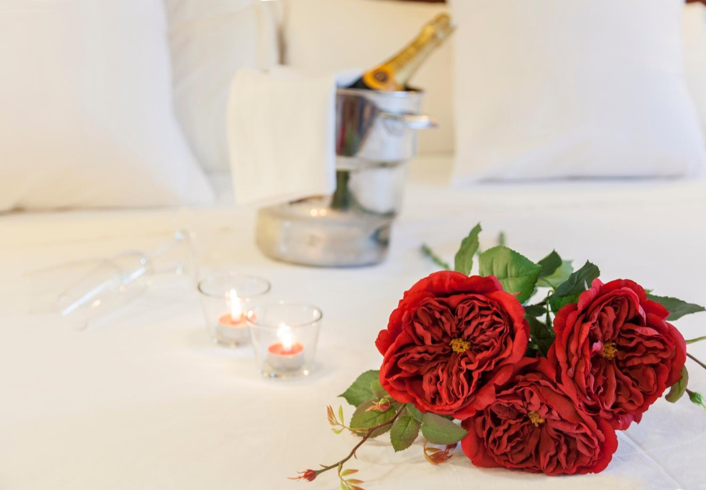 A table with a bouquet of red flowers, a champagne bottle, and two lit candles.