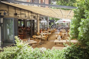 An outdoor cafe with tables and chairs, covered by a canopy, and surrounded by greenery. - Hospedium Hotel Los Lanceros (San Lorenzo de El Escorial)