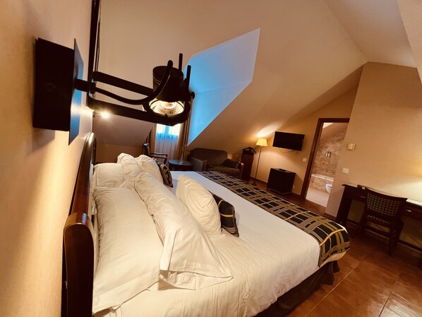 A bedroom with a large bed, a desk, a chair, a TV, and a lamp.