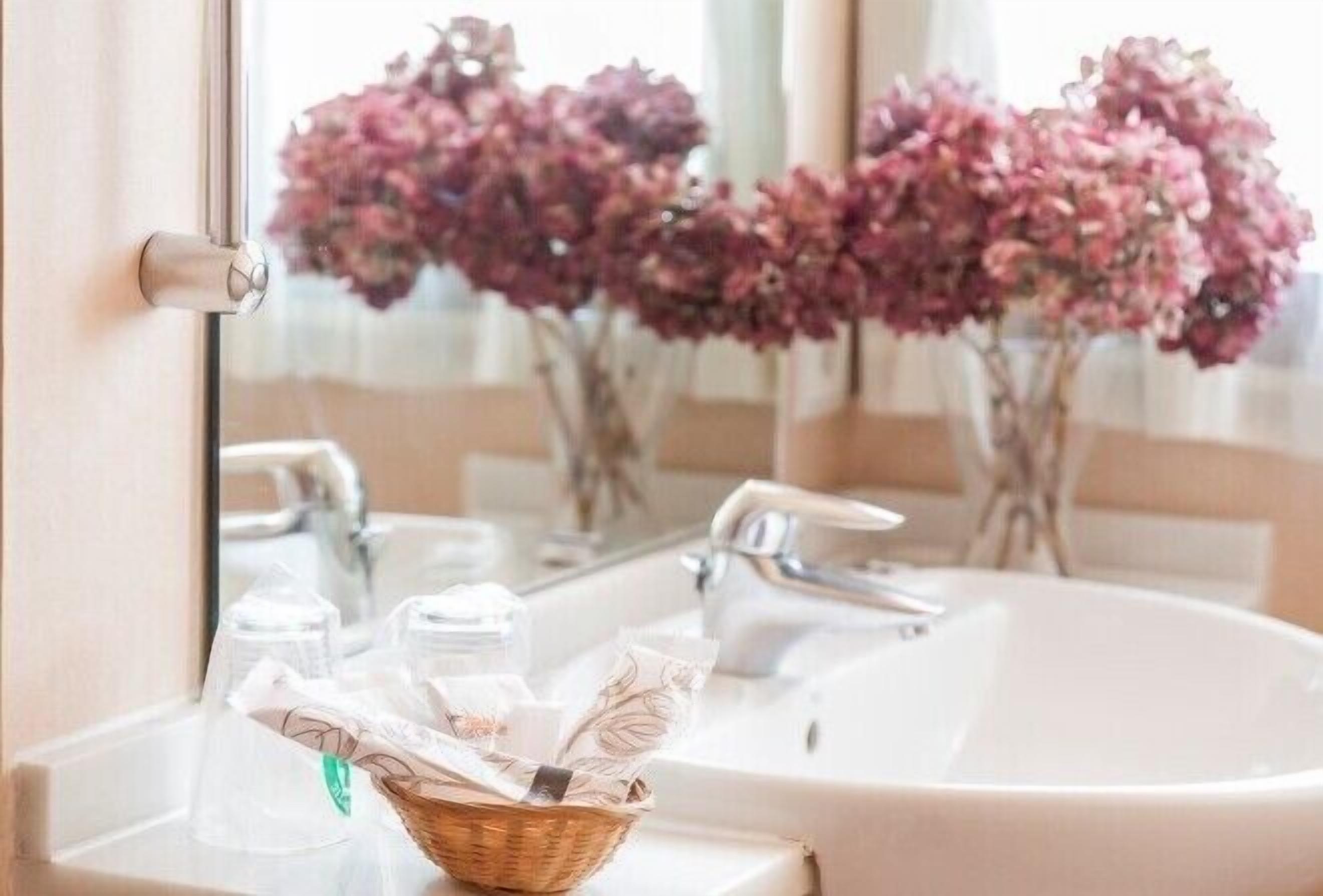Un baño con un lavamanos blanco, un espejo y una cesta de mimbre en la encimera.