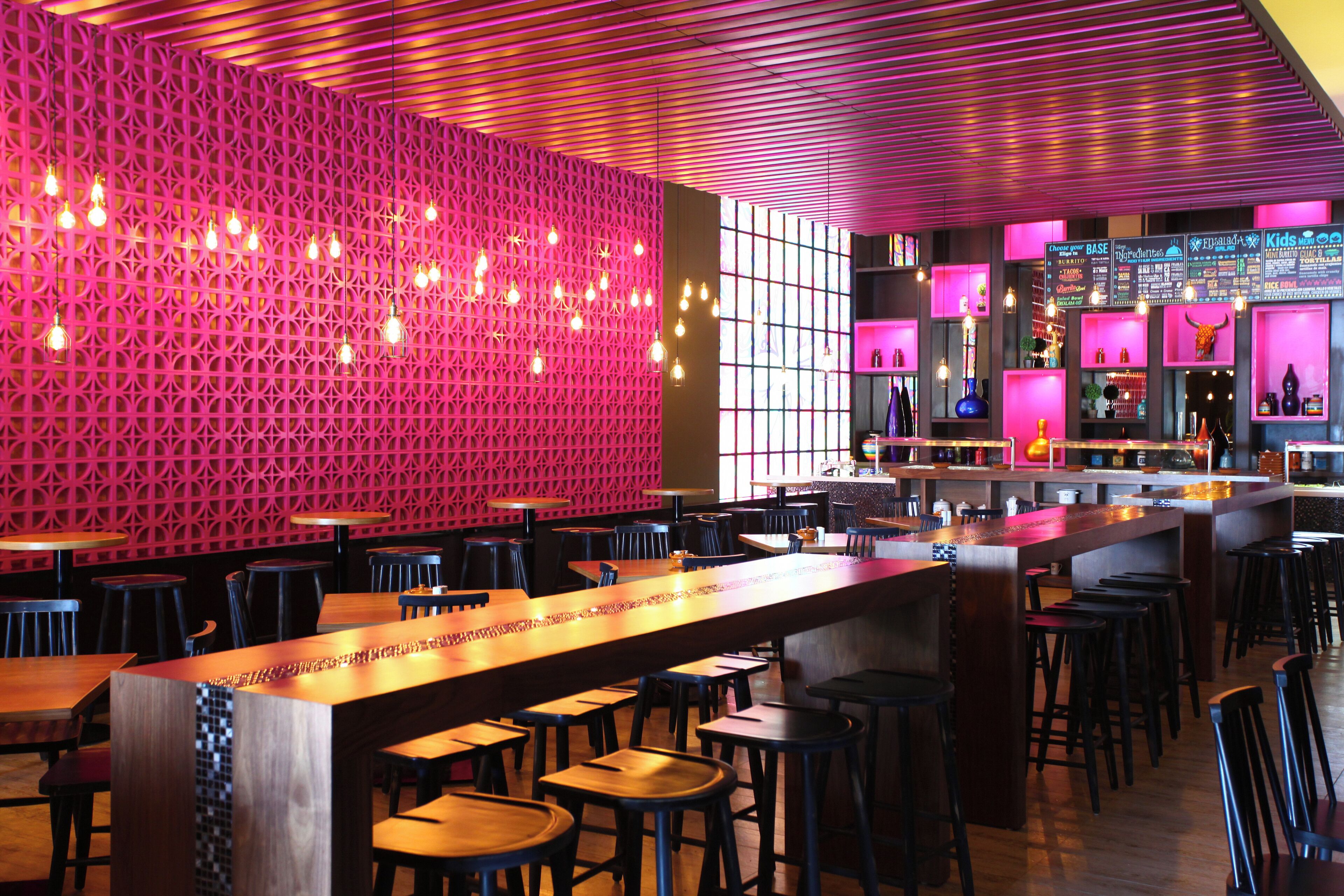 Een moderne bar met een rode geometrische wand, een houten bar en verschillende krukken.