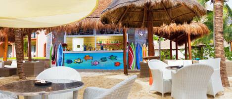 A beachside bar area with wicker furniture, a thatched umbrella, and colorful surfboards.