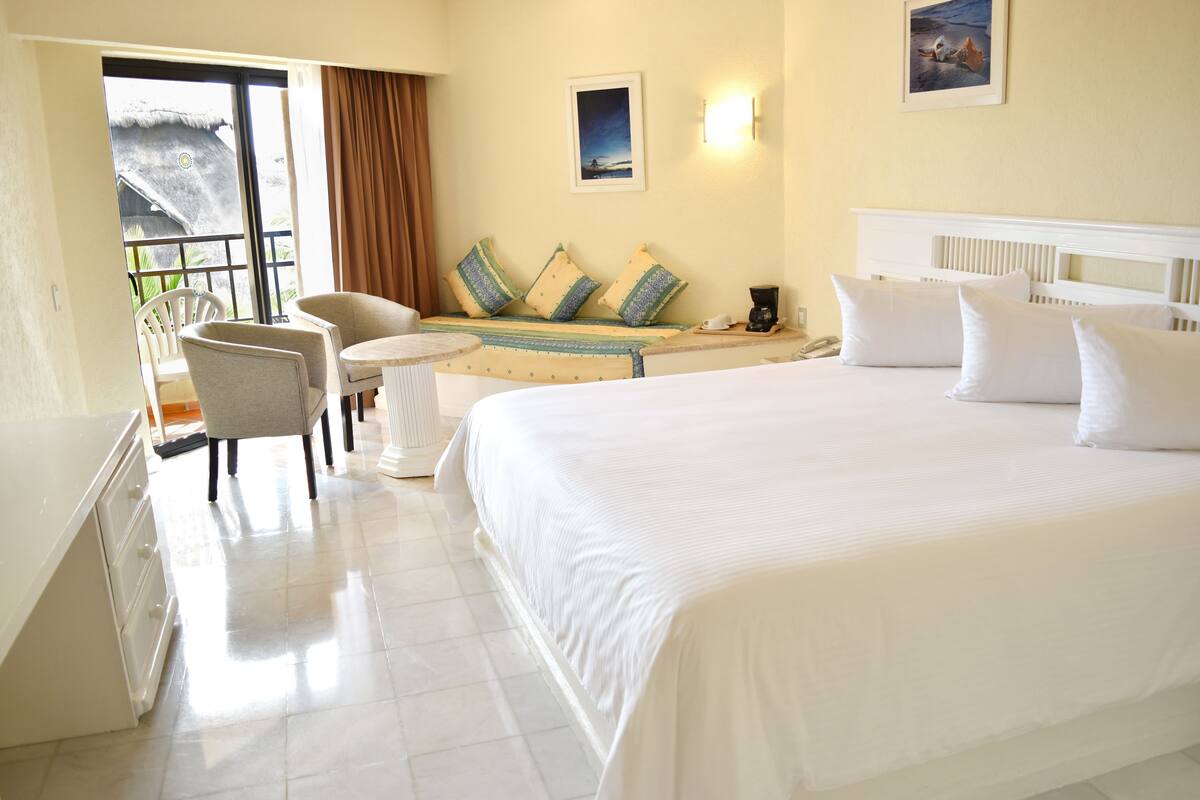 Une chambre d’hôtel dotée d’un grand lit, d’un coin salon avec une table et des chaises, et d’un balcon avec vue.