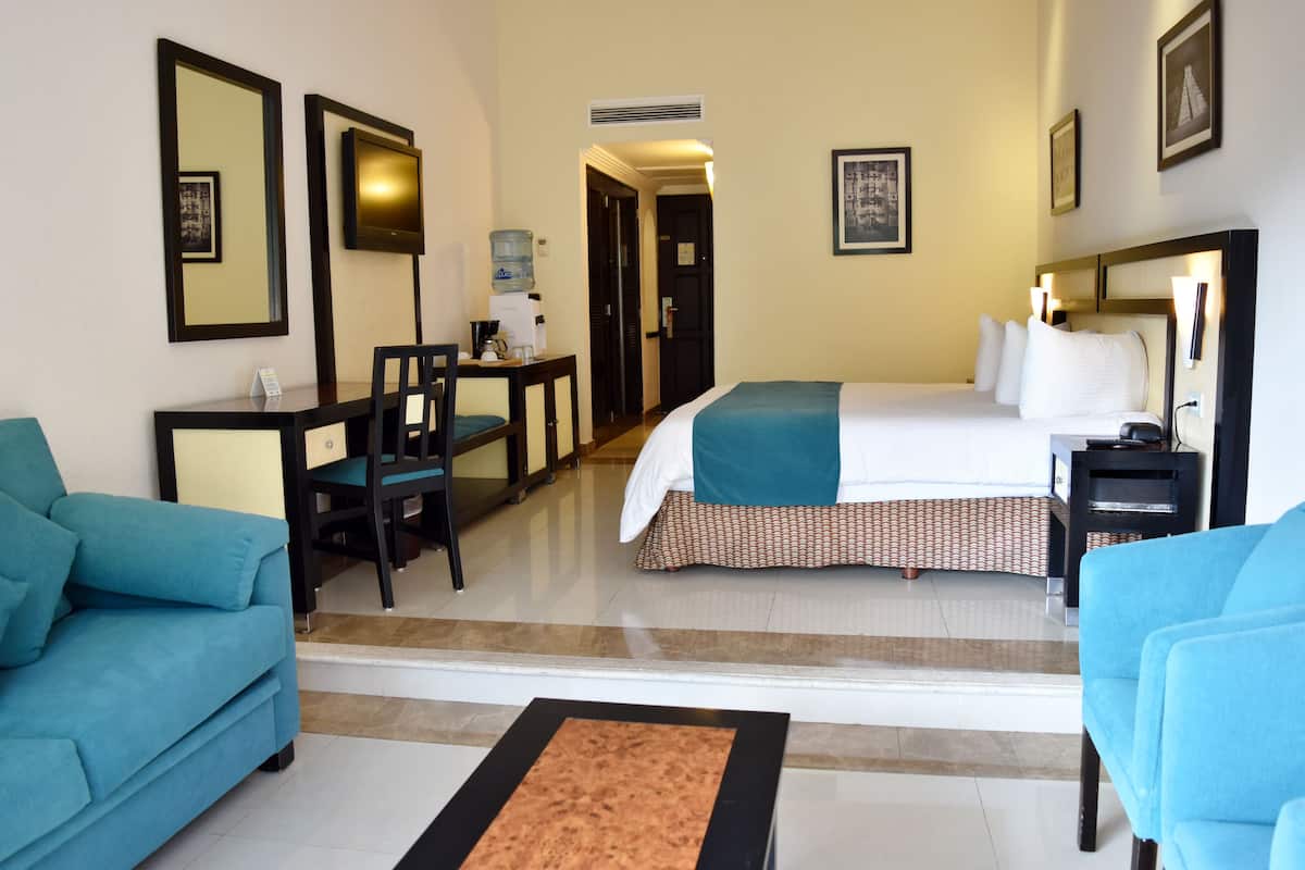 Une chambre d’hôtel comprenant un lit, deux fauteuils bleus, un bureau avec une chaise, un distributeur d’eau et un téléviseur.