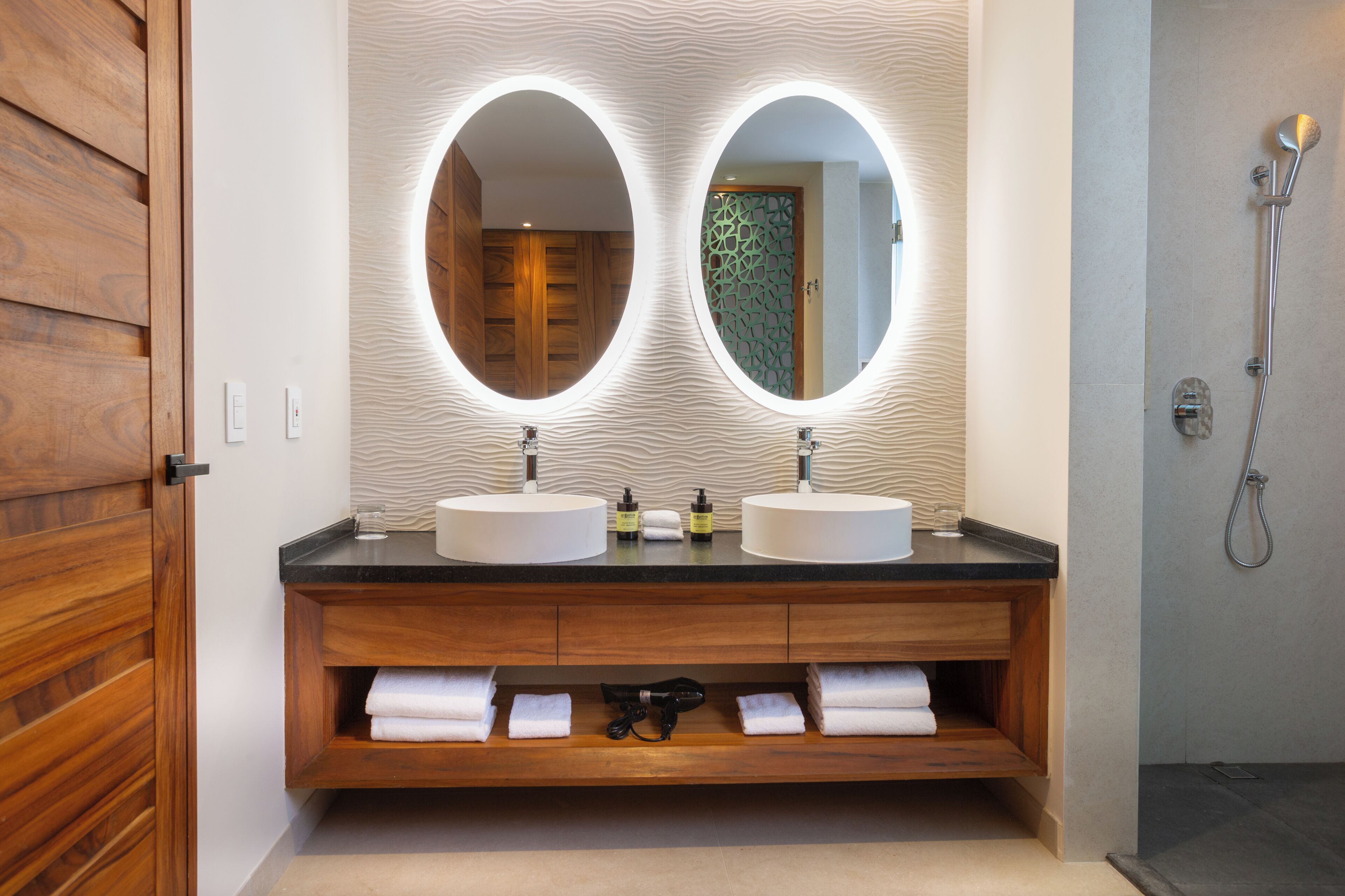 Un baño con dos espejos redondos, tocador de madera y ducha.