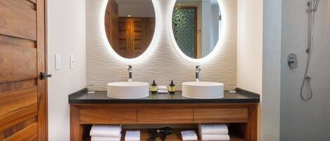 A bathroom with two round mirrors, wooden vanity, and a shower.