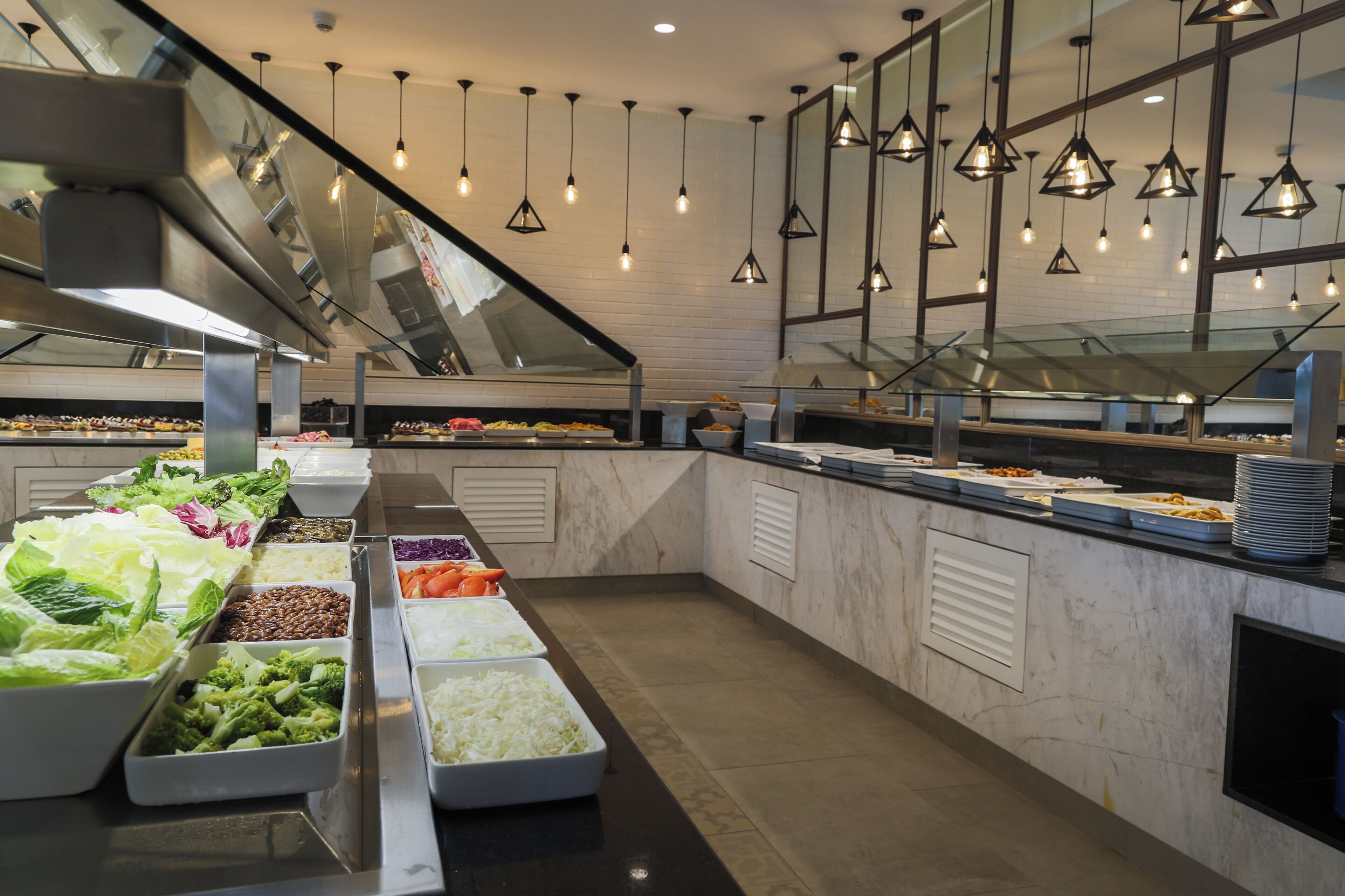 Un área de bufé con diferentes estaciones de comida, que incluyen ensaladas, cereales y verduras.