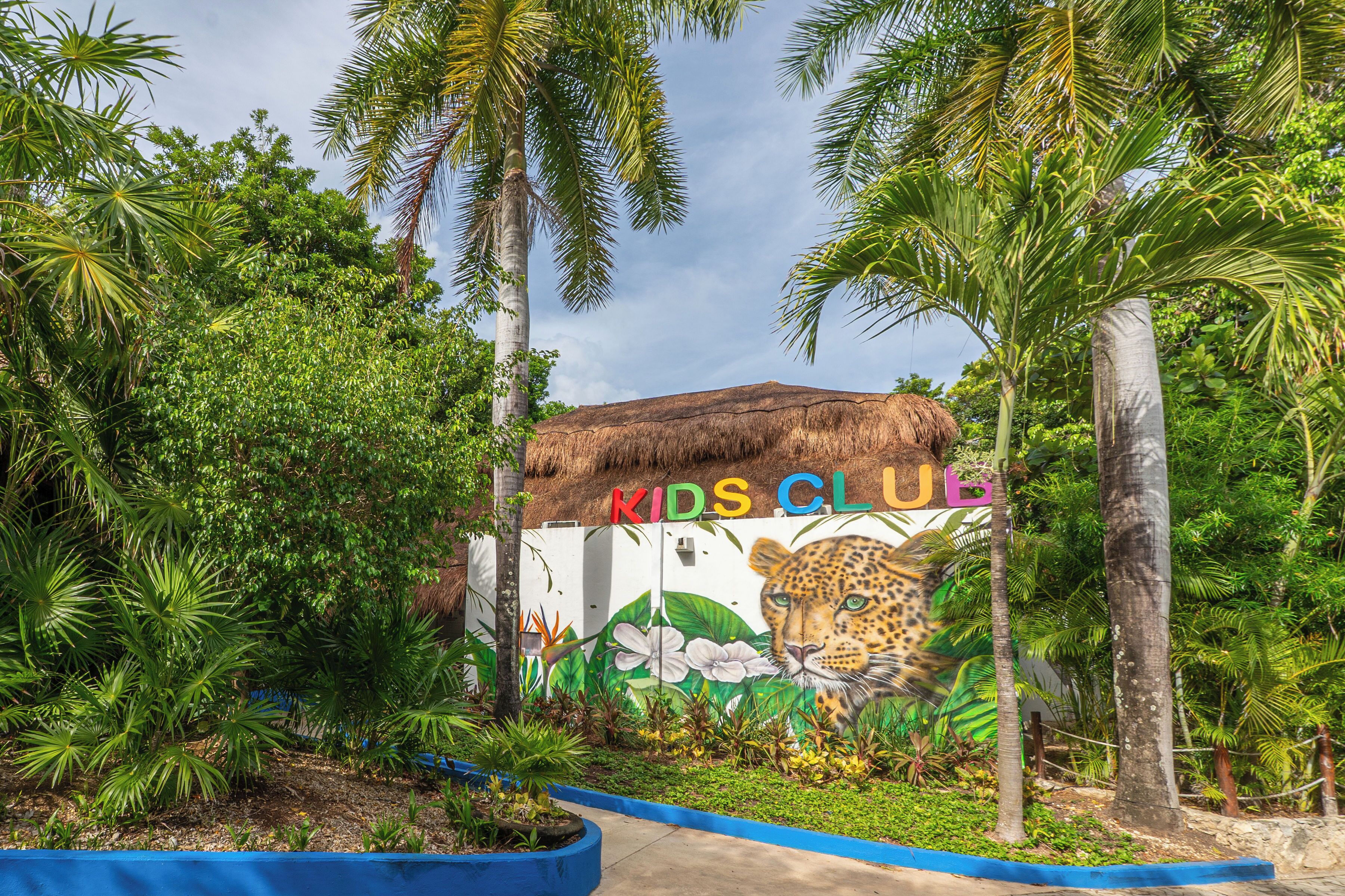Una entrada con temática tropical que presenta un mural de un leopardo y las palabras 'KIDS CLUB' en un edificio.